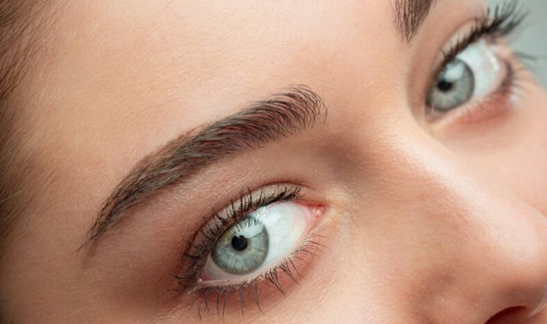 Naheaufnahme eines Gesichts mit betonten Augenbrauen und strahlend blauen Augen.